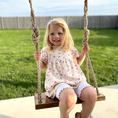 Load image into Gallery viewer, child using walnut swing shown in child size installed with brown rope on outdoor patio area
