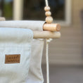 Load image into Gallery viewer, close up of maple wood dowel and bead details on premium outdoor toddler swing in wheat, set up on outdoor patio with twisted vanilla ropes