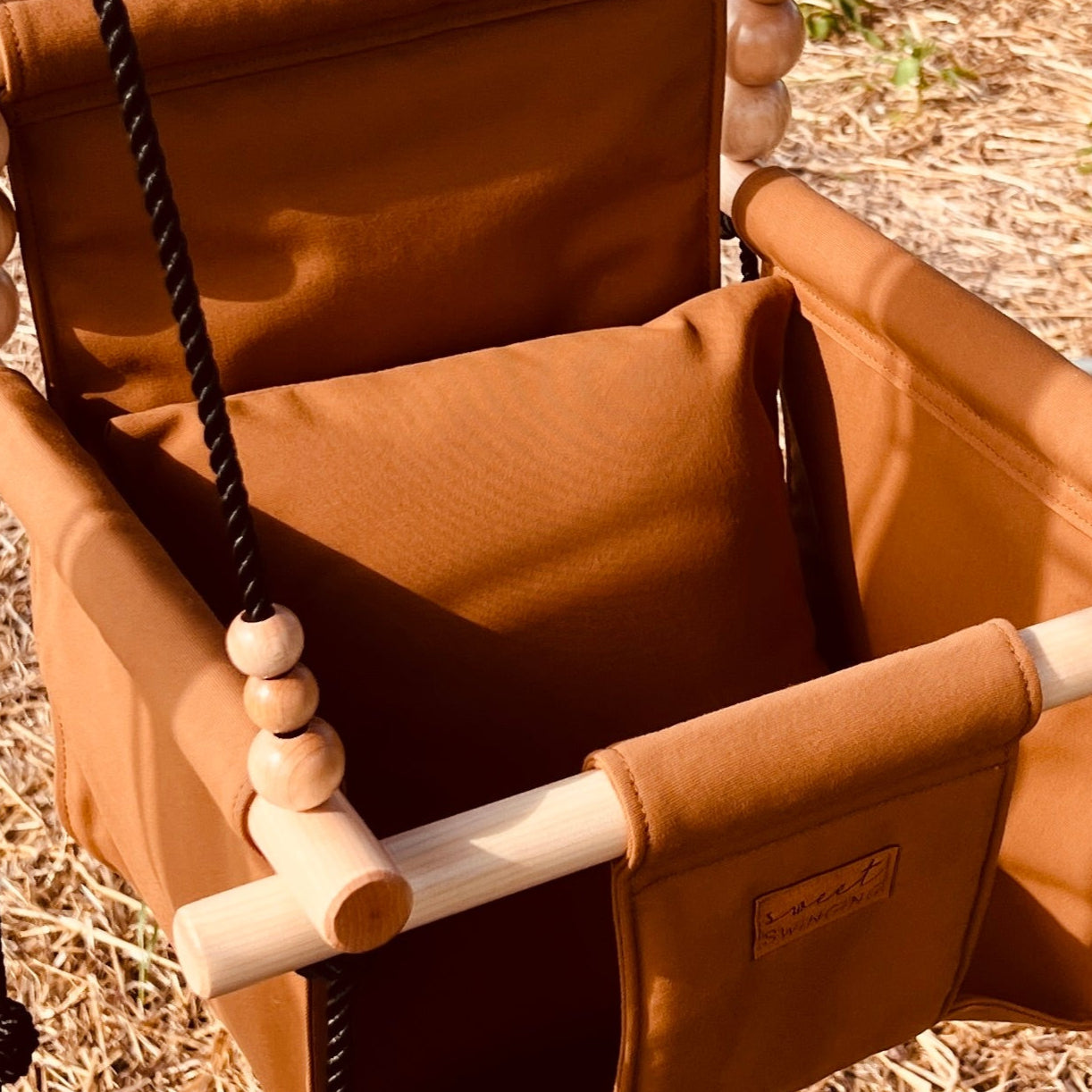 Brown swing chair hanging outdoors with a rural landscape in the background
