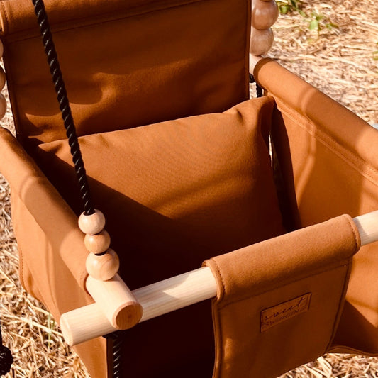 Brown swing chair hanging outdoors with a rural landscape in the background