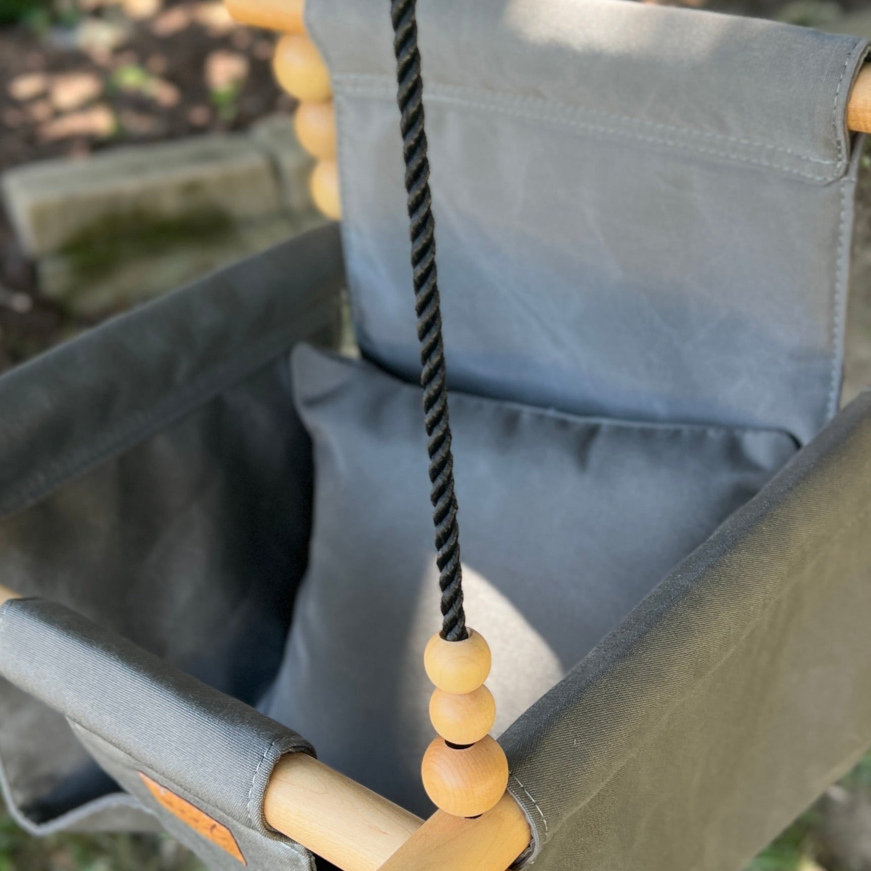 Children's swing with gray seat and wooden handles in a garden setting