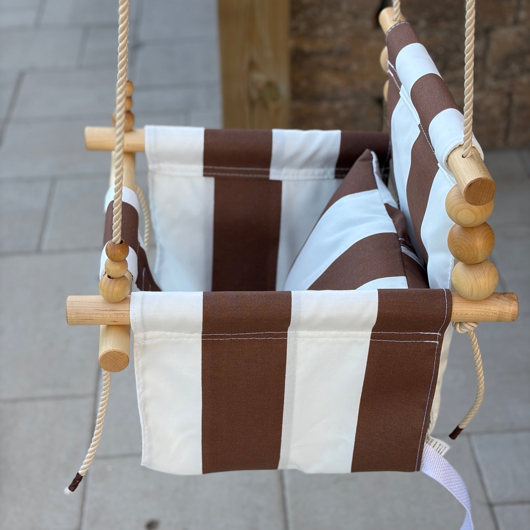 Children's swing with brown and white striped seat shown with vanilla twisted rope and 1 pillow