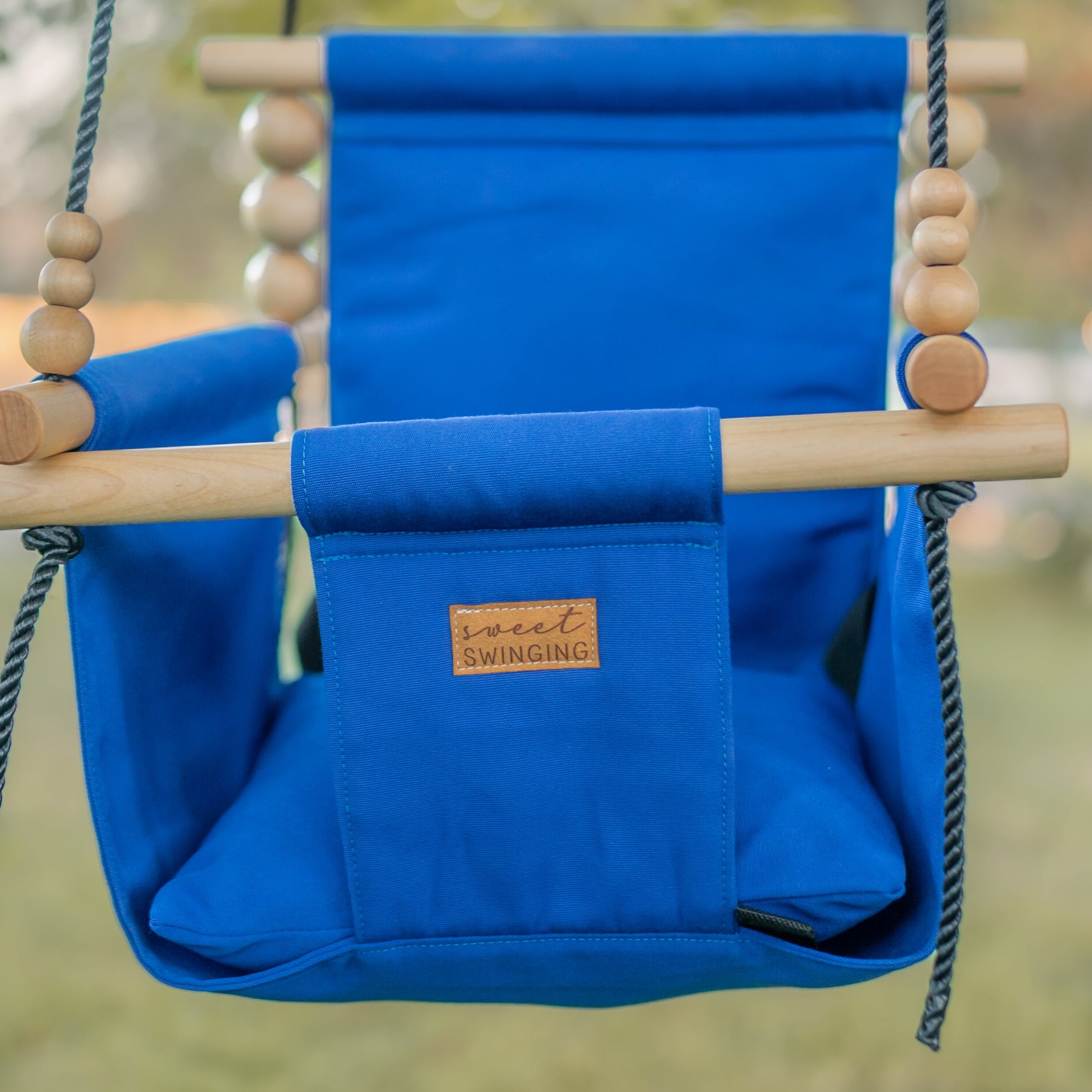 Blue children's swing with wooden frame and ropes, set against a blurred natural background.