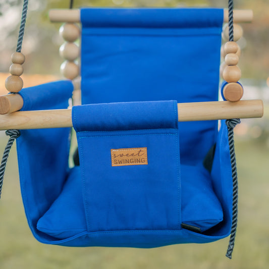 Blue children's swing with wooden frame and ropes, set against a blurred natural background.