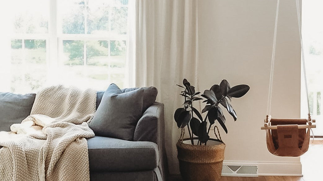 Living room with a gray sofa, plant, and swing by a window