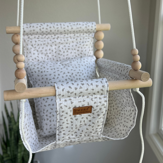 Neutral confetti baby swing with soft speckled pattern, shown with 1 pillow, safe indoor use