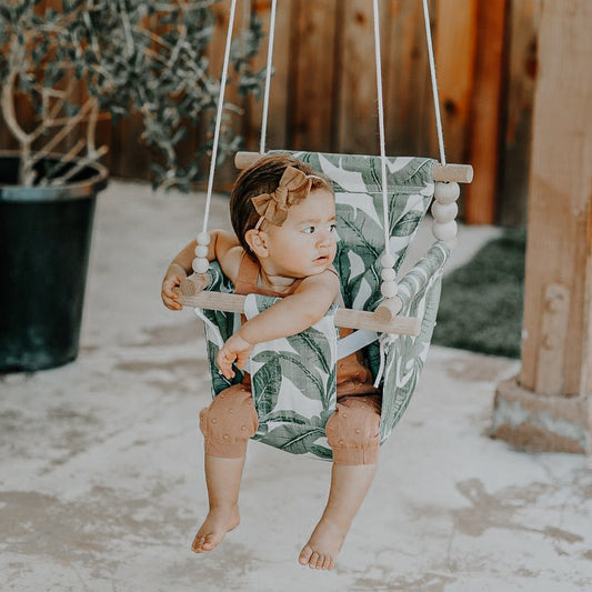 Baby using tropical leaf outdoor baby swing shown with white braided rope