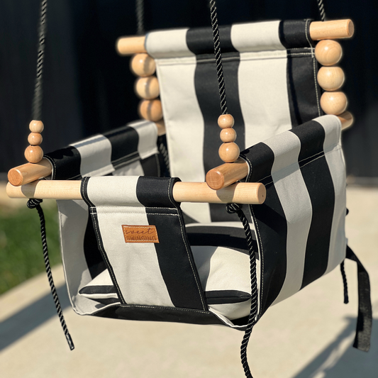 Side view of wide black striped pattern outdoor high back baby swing with beautiful maple wood dowels and black twisted rope