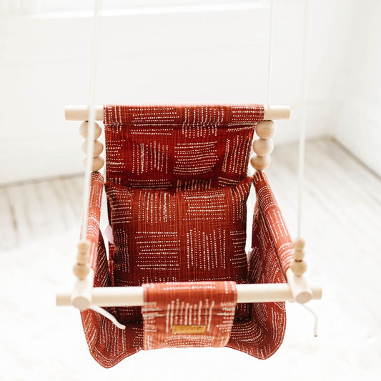 Front view brick red baby swing with high back support, rustic indoor cotton design shown with one pillow